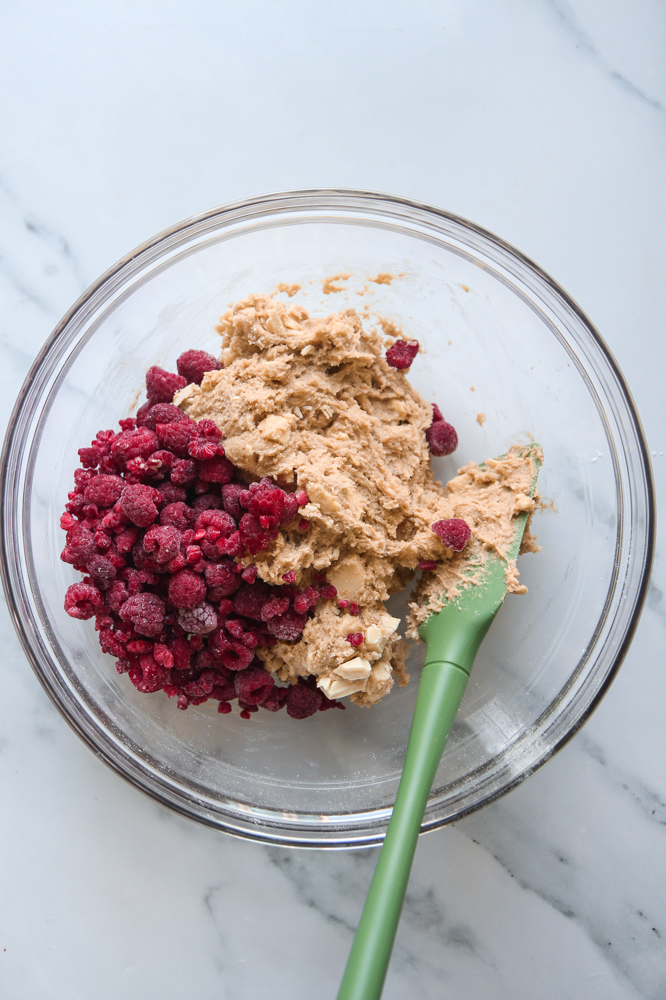 A bowl of cookie dough with a pile of frozen raspberries on top.