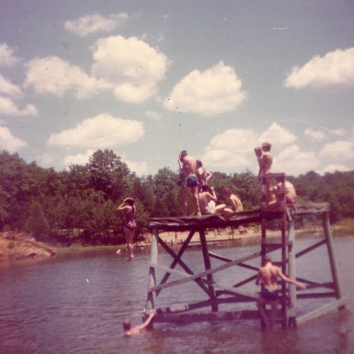 People jumping off a dock into a lake.