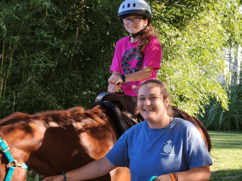 Two girls on a brown horse at camp.