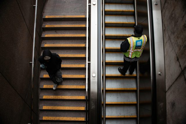 Pendler bewÃ¤ltigen Rolltreppen und Treppen in einer U-Bahn-Station in San Francisco mit Sicherheitspersonal.
