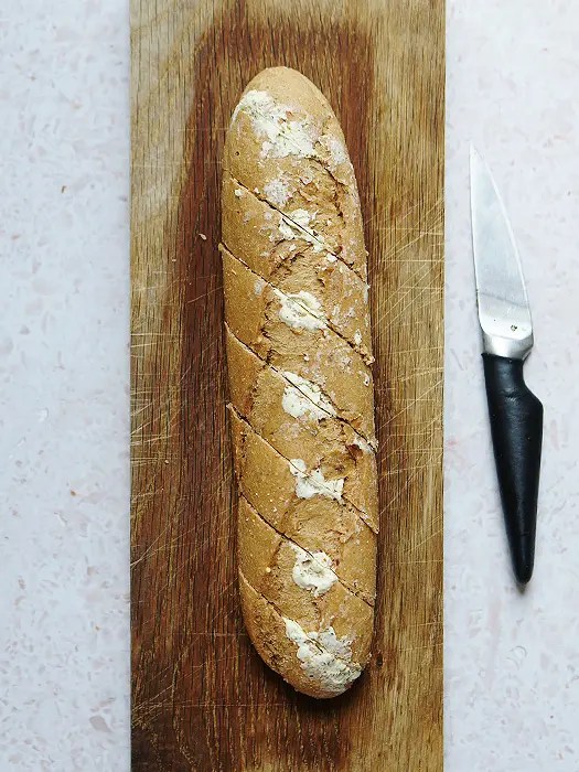 Kräuterbaguette auf einem Holzbrett, daneben ein Messer zum Einschneiden.