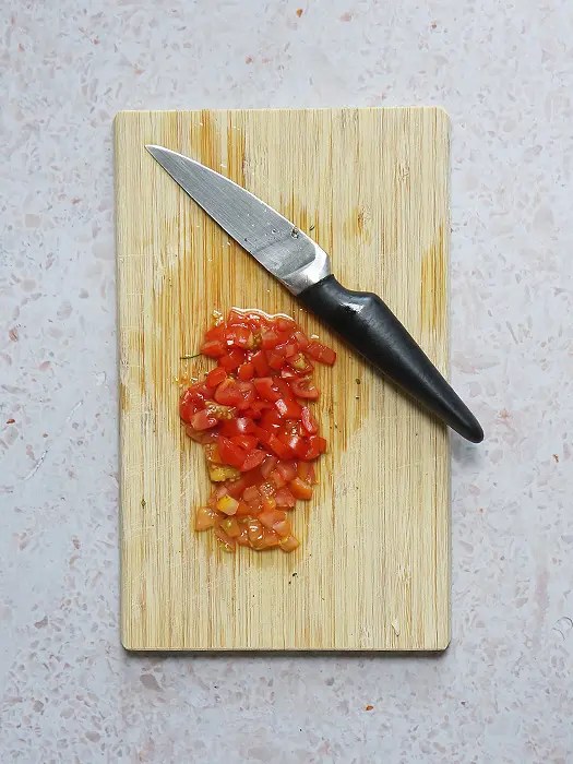 Tomaten auf einem Holzbrett, fein gewürfelt für das gefüllte Kräuterbaguette.