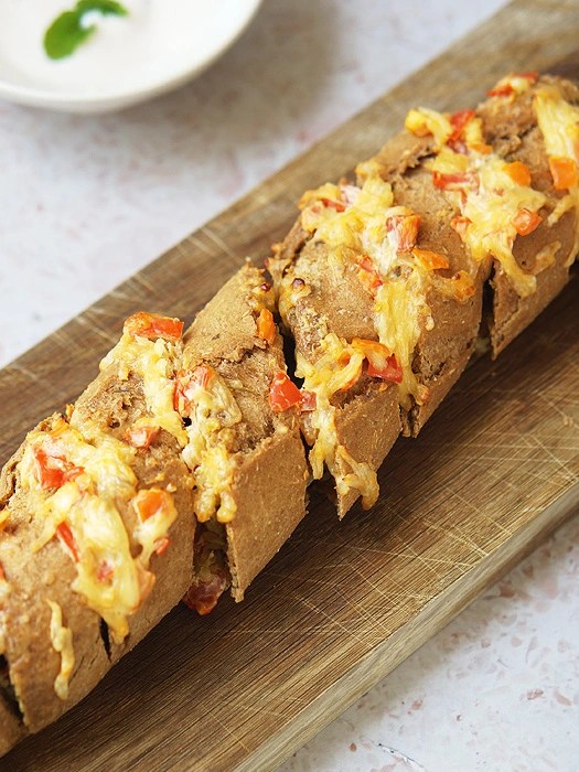 Kräuterbaguette mit Käse und Tomaten gefüllt auf einem Holzbrett.