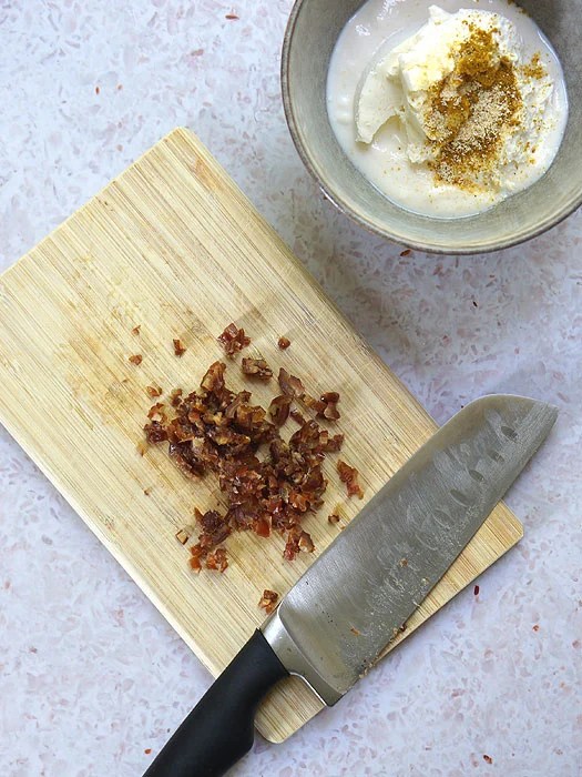 Gehackte Datteln auf einem Holzbrett und Frischkäse mit Curry in einer Schale.
