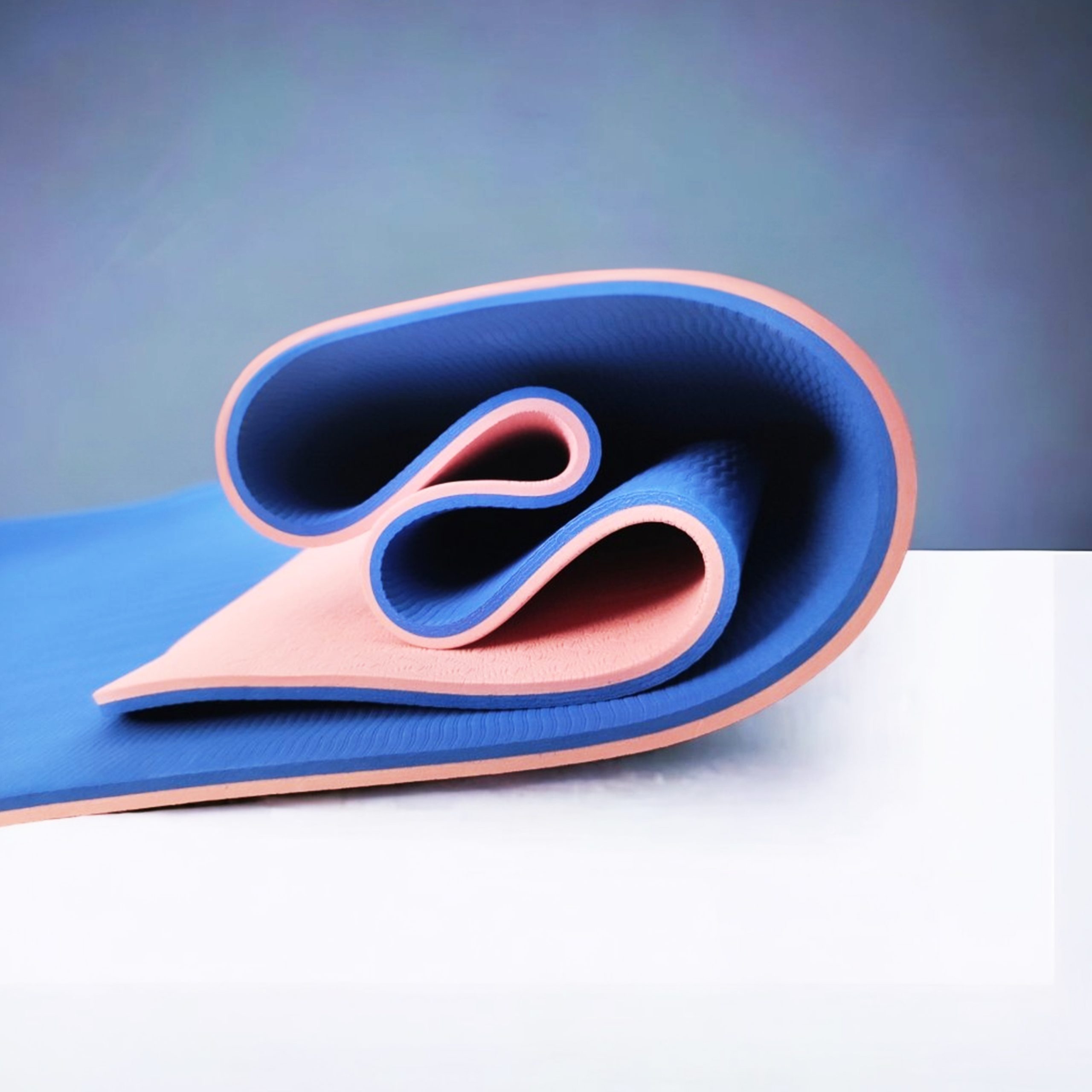 Partially unrolled blue and pink yoga mat on a white surface.
