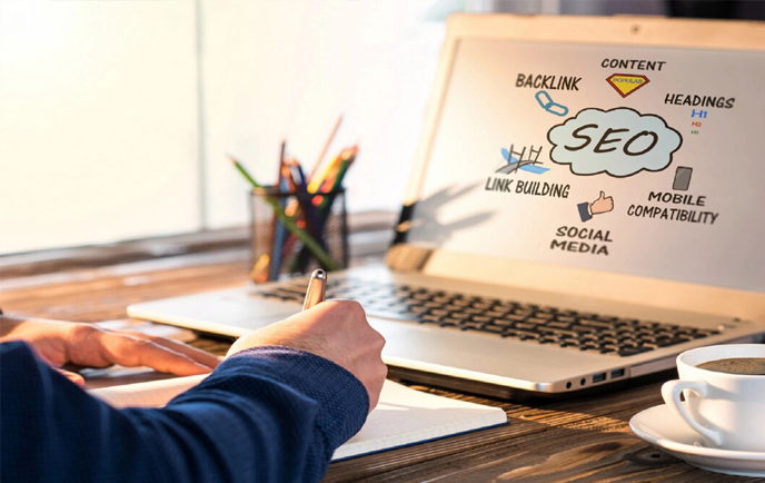 Person writing notes with a laptop displaying an SEO concept map.