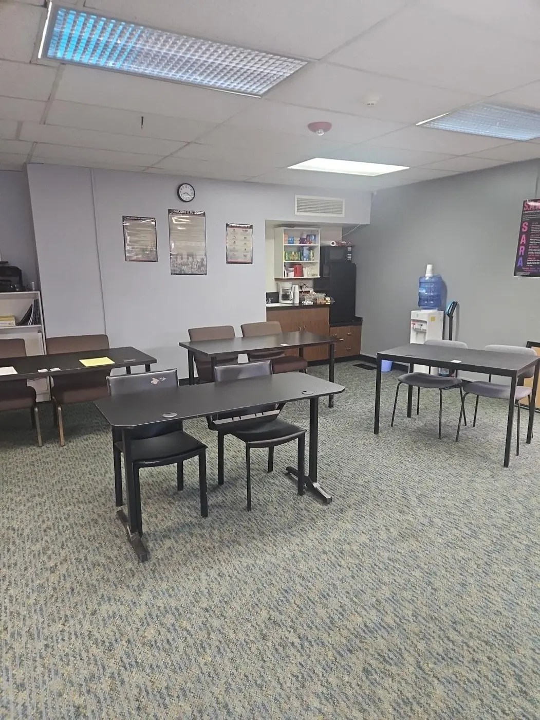 OTS Security Training classroom student area with tables, chairs, legal-reference posters, refreshment station, refrigerator, and water dispenser