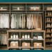 A clean lifestyle hero photograph of a fully organized walk-in closet styled in warm oat and deep sage tones, featuring a double hang rod with neatly arranged clothes, labeled shelf sections, and an angled shoe rack in soft, natural lighting.