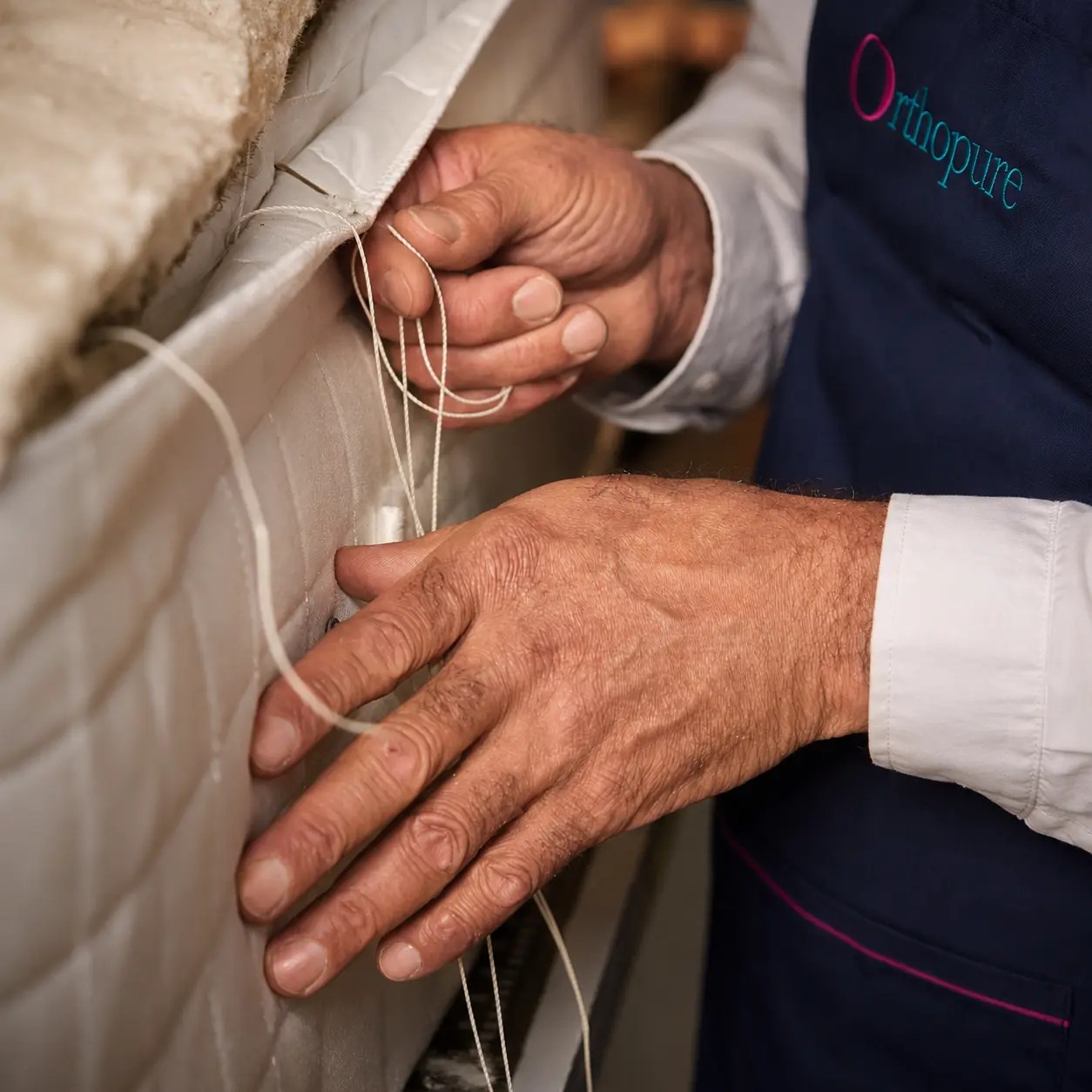 A tradesman hand side side stitching a mattress