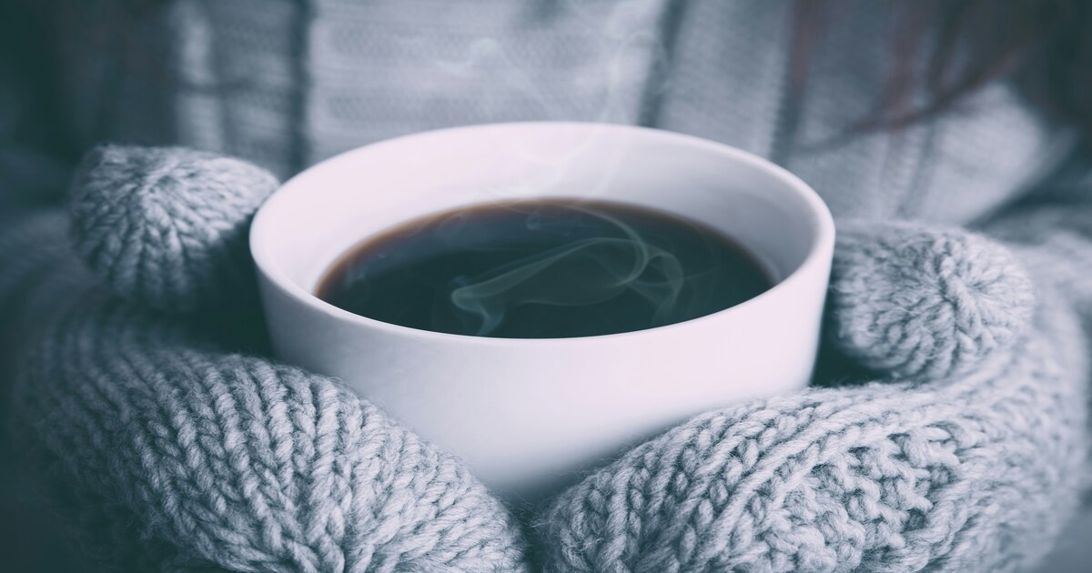 Person wearing gray mittens holding a cup of hot coffee
