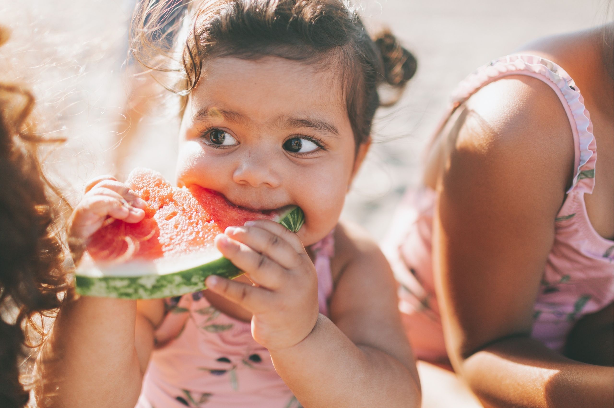 A little girl happily eating a slice of watermelon on a sunny day, with juice dripping down her chin