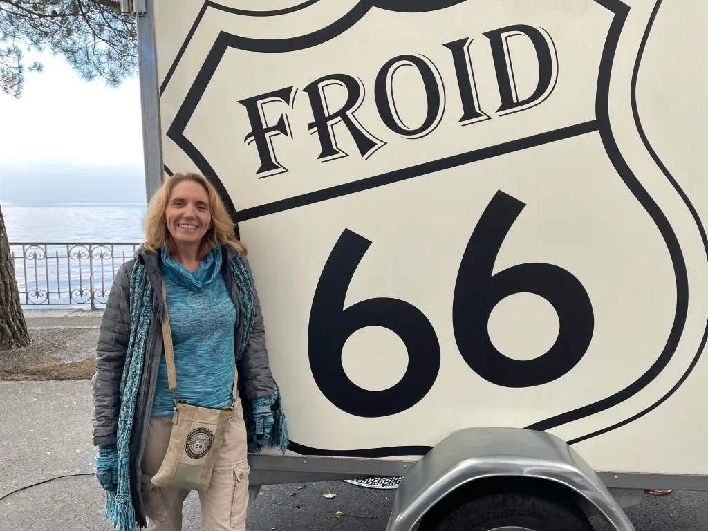 Smiling woman standing next to a large Route 66 sign near the Lake Geneva waterfront with trees and railing