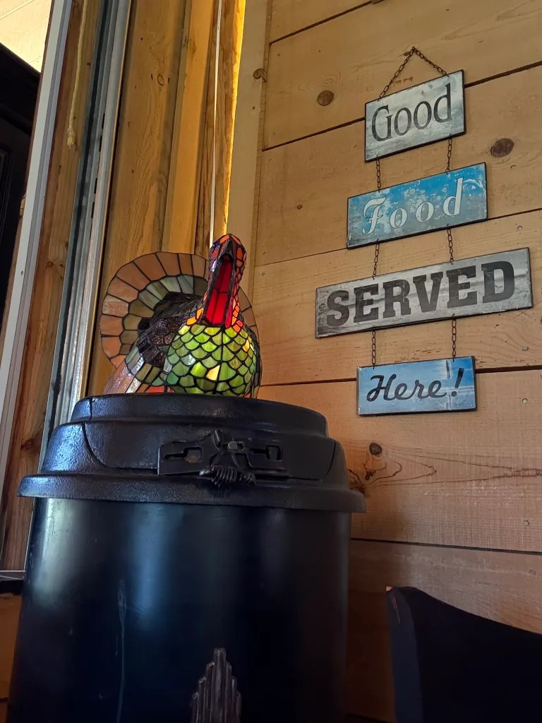 A glass chicken sits on a potbellied stove near a metal sign reading "Good food served here."