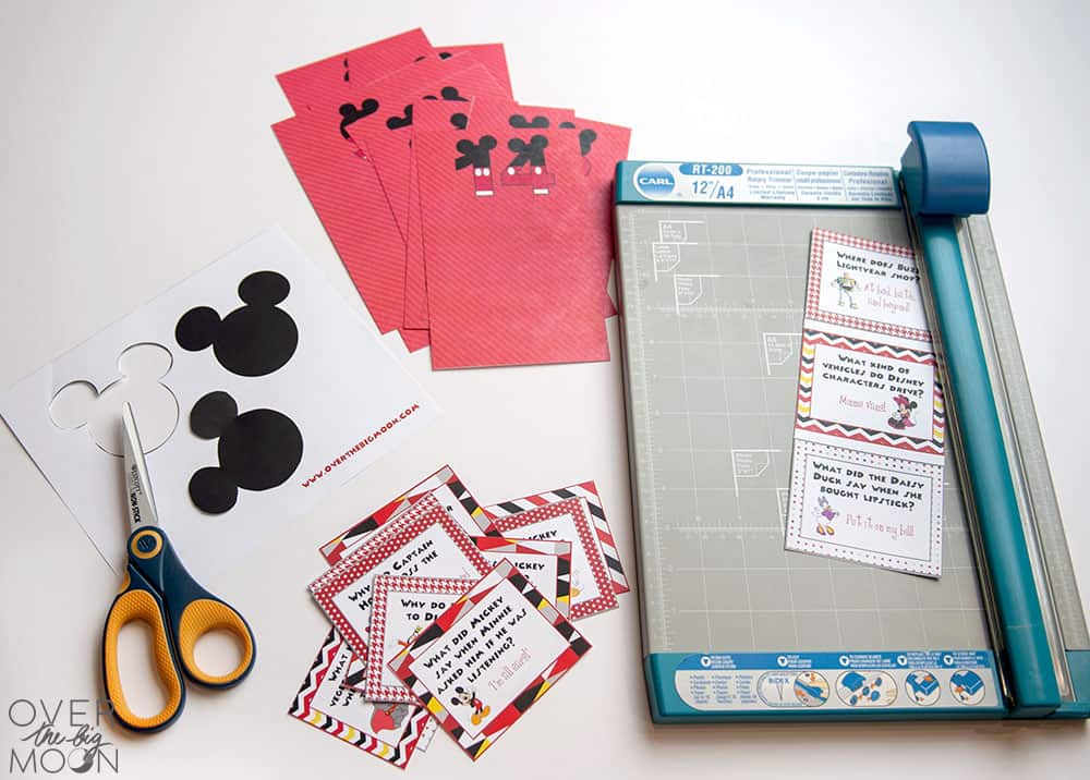 Cut up printed Disney Joke Cards and Red envelopes next to a paper trimmer.