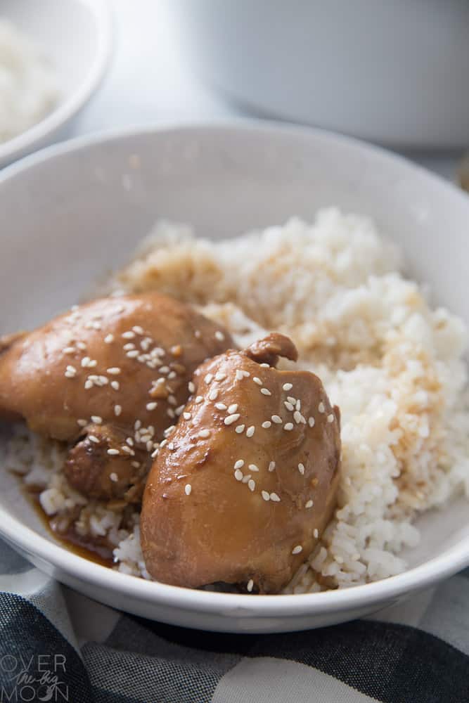 A couple bone-in, garlic chick thighs, in a white plate bowl next to some white rice.