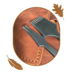Handmade An oval shape with a close up image of a copper tone leather with punch marks. Two stitching chisels rest on top of the leather. The oval is surrounded by a golden yellow oak leaf and feather.