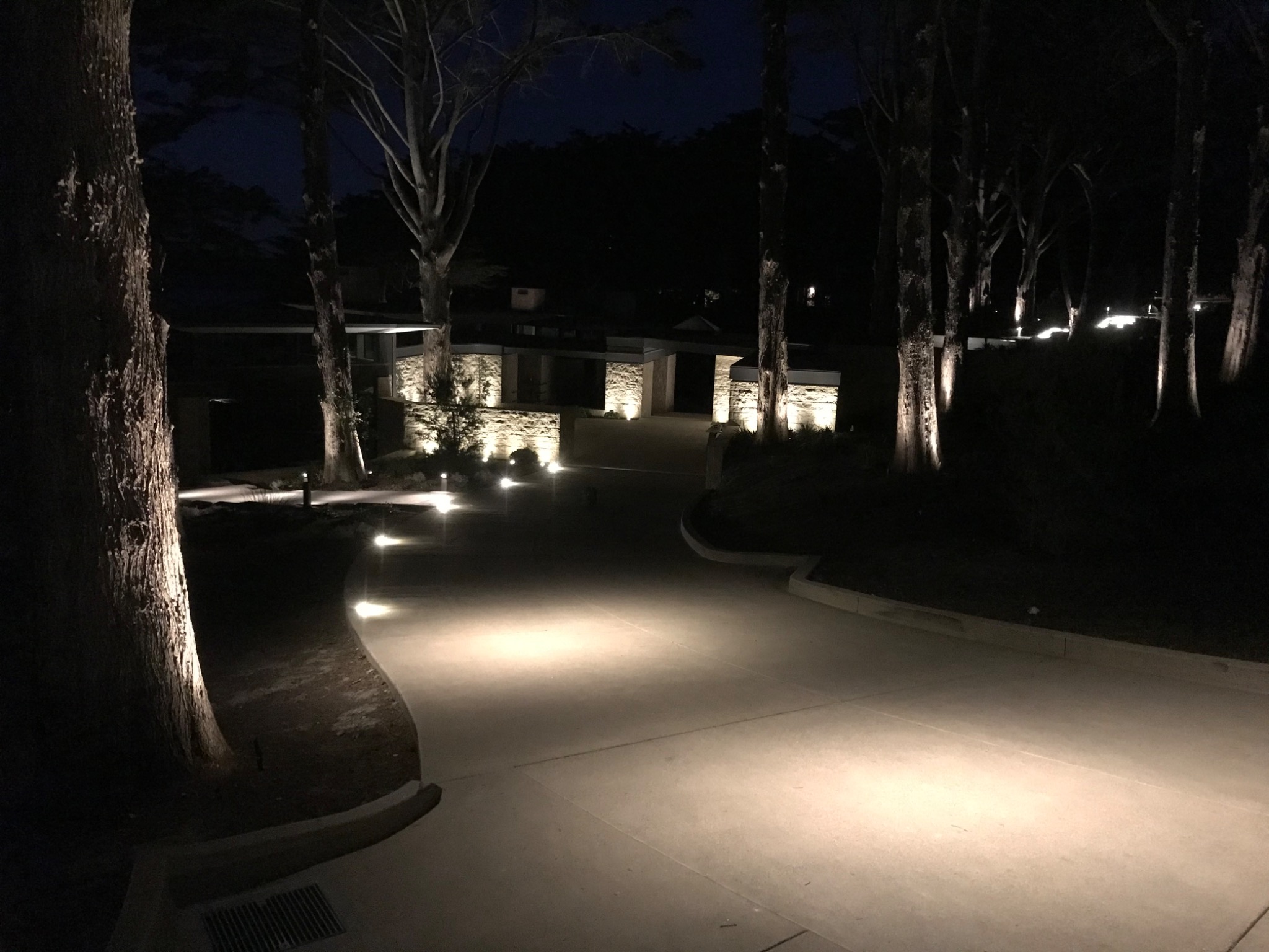 Custom landscape lighting along a driveway, stone walls, and trees at night