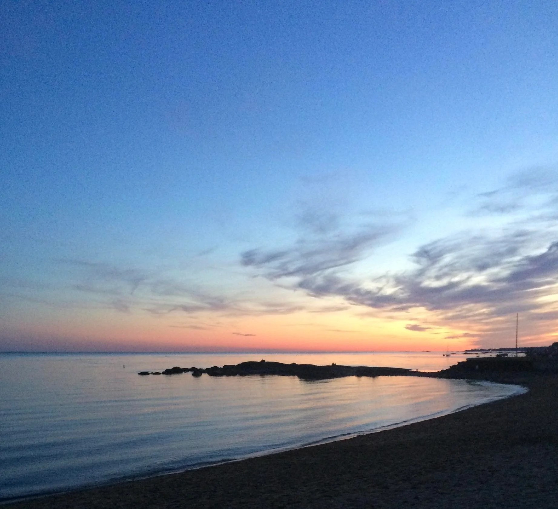 Sunset over the calm waters at Madison Surf Club Beach in Connecticut, with soft waves and glowing sky.