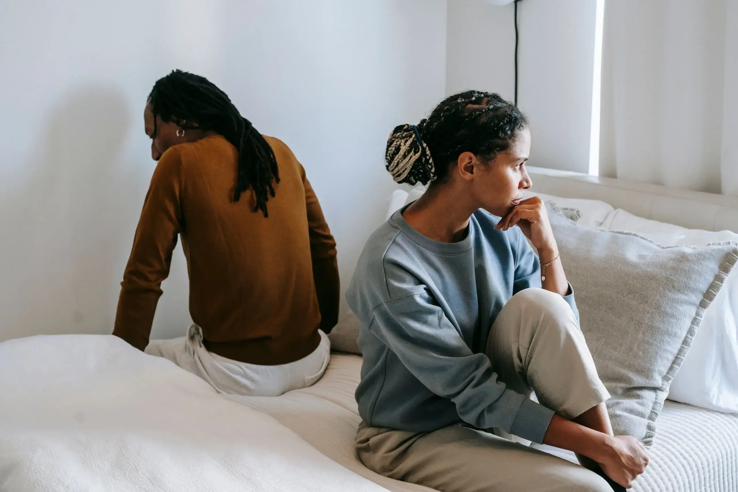 A couple sitting apart on a bed after an argument, illustrating the emotional distance and relationship challenges often experienced by people with Complex PTSD (CPTSD).