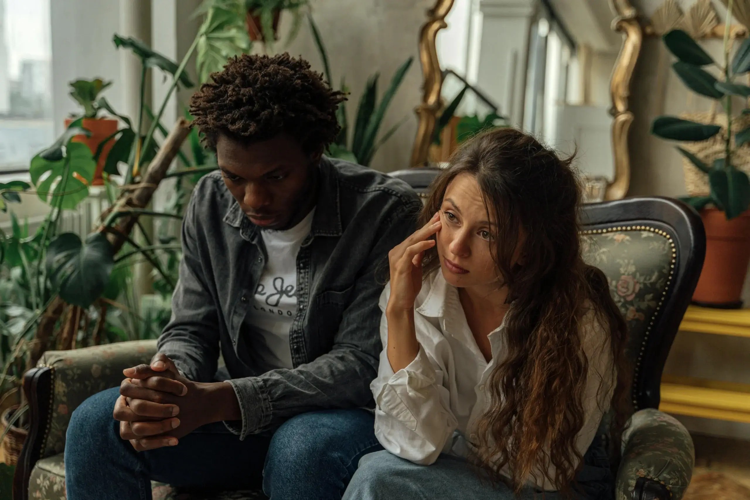 Couple sitting together looking distressed and reflective as they navigate underlying emotions and relationship challenges during a difficult conversation.