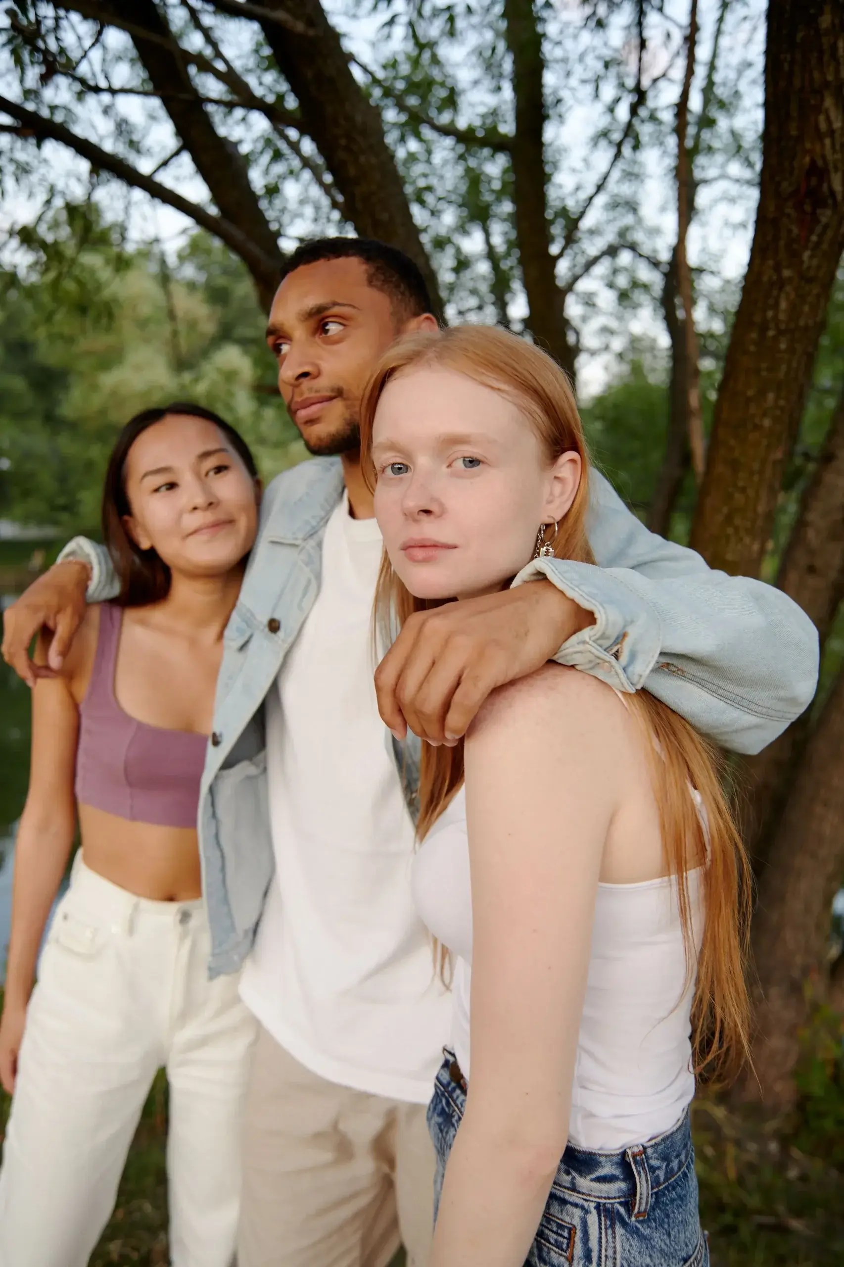 Three partners in a polyamorous relationship stand together outdoors, representing trust, connection, and relationship therapy for ethically non-monogamous relationships.