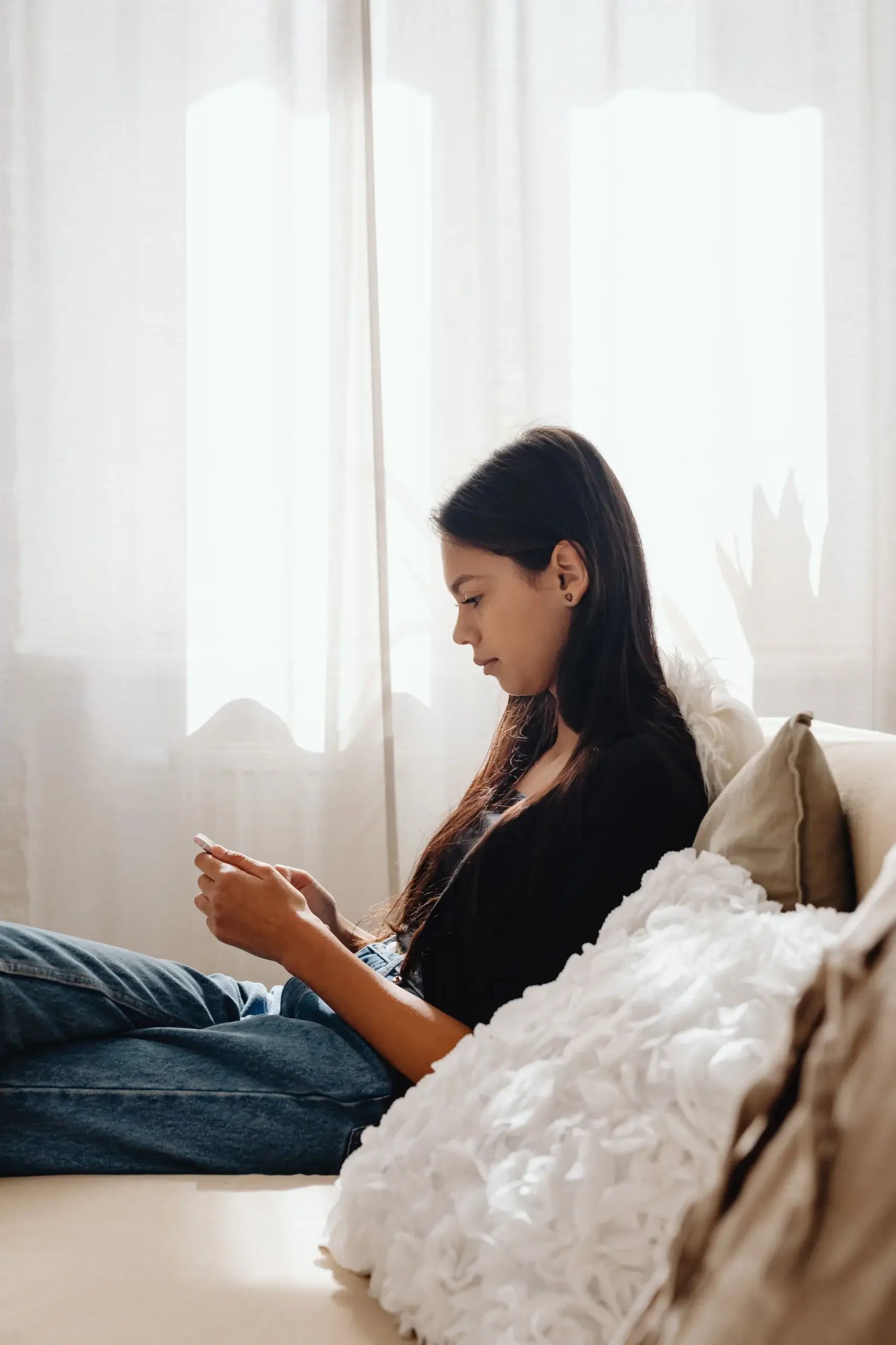 Woman sitting quietly by a sunlit window, reflecting alone on a couch