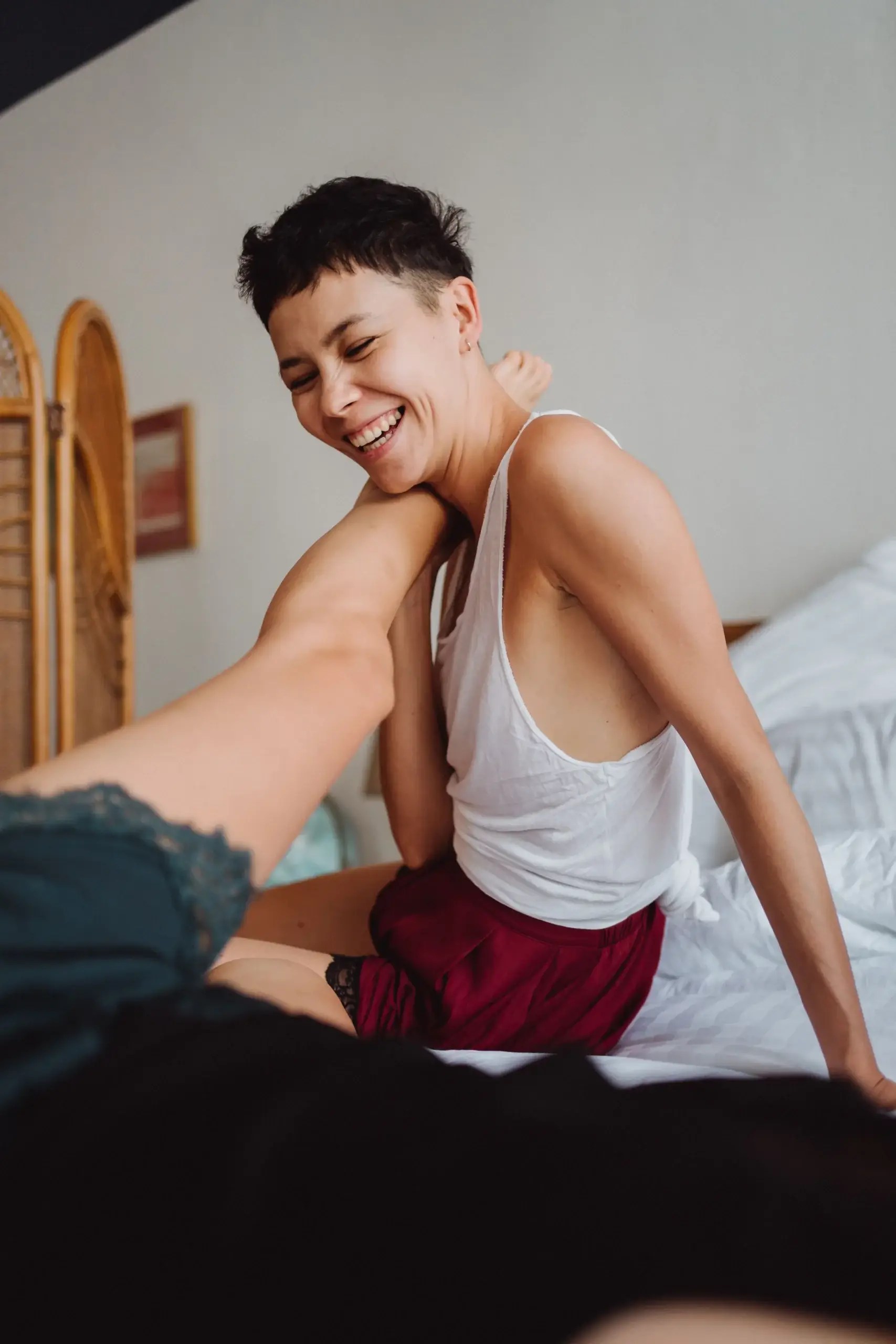 Smiling partner sitting on a bed with their partner, sharing a playful and affectionate moment.
