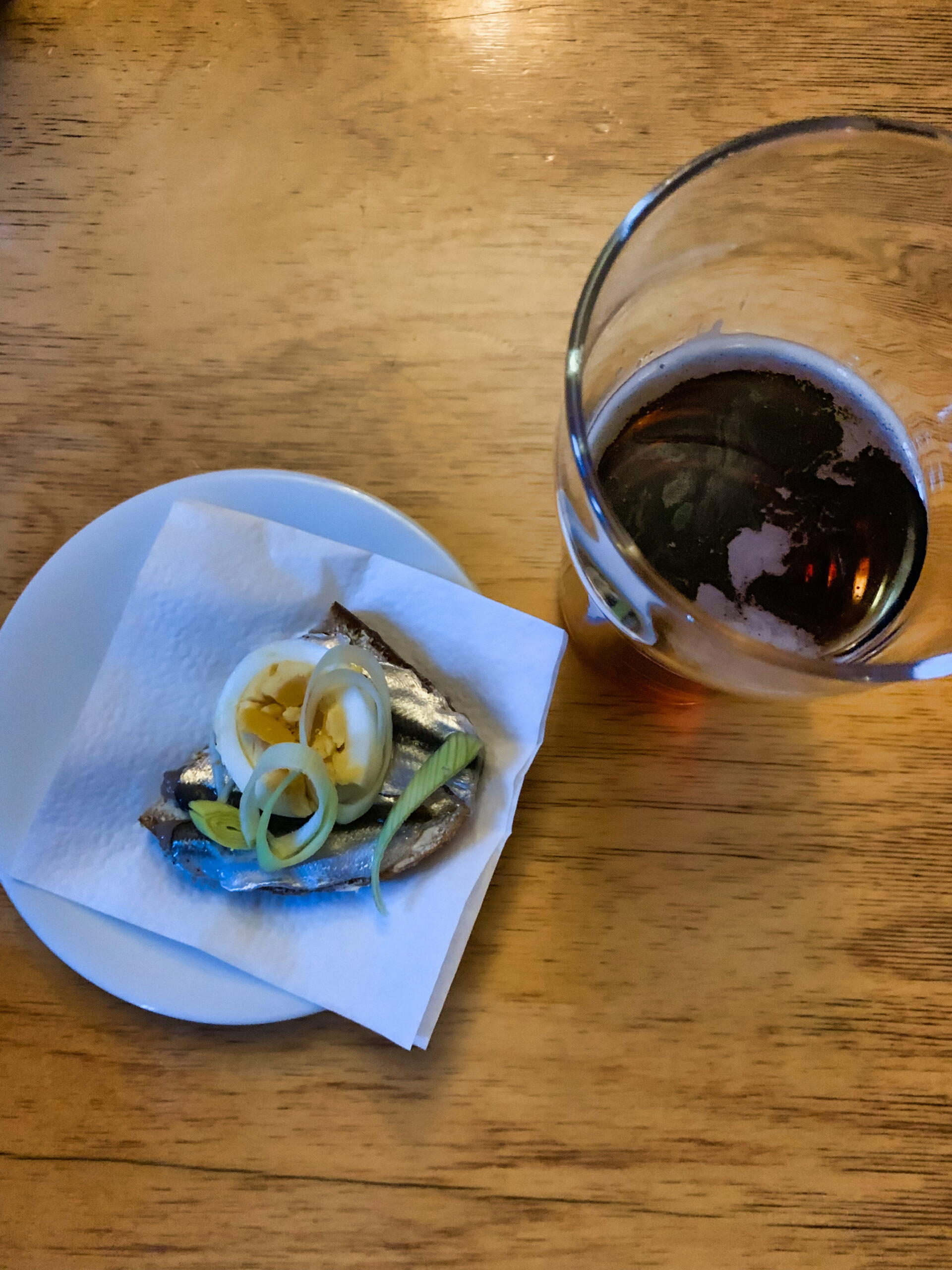 Silakkavoileipä keitetyllä kananmunalla ja ruohosipulilla lautasella sekä lasillinen tummaa olutta pöydällä