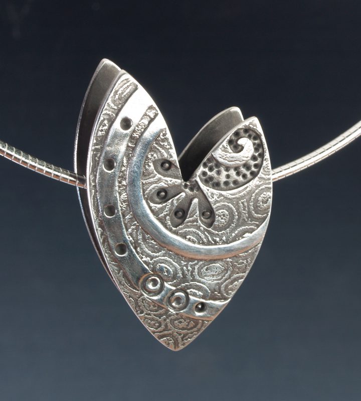 Silver heart-shaped pendant with intricate designs.