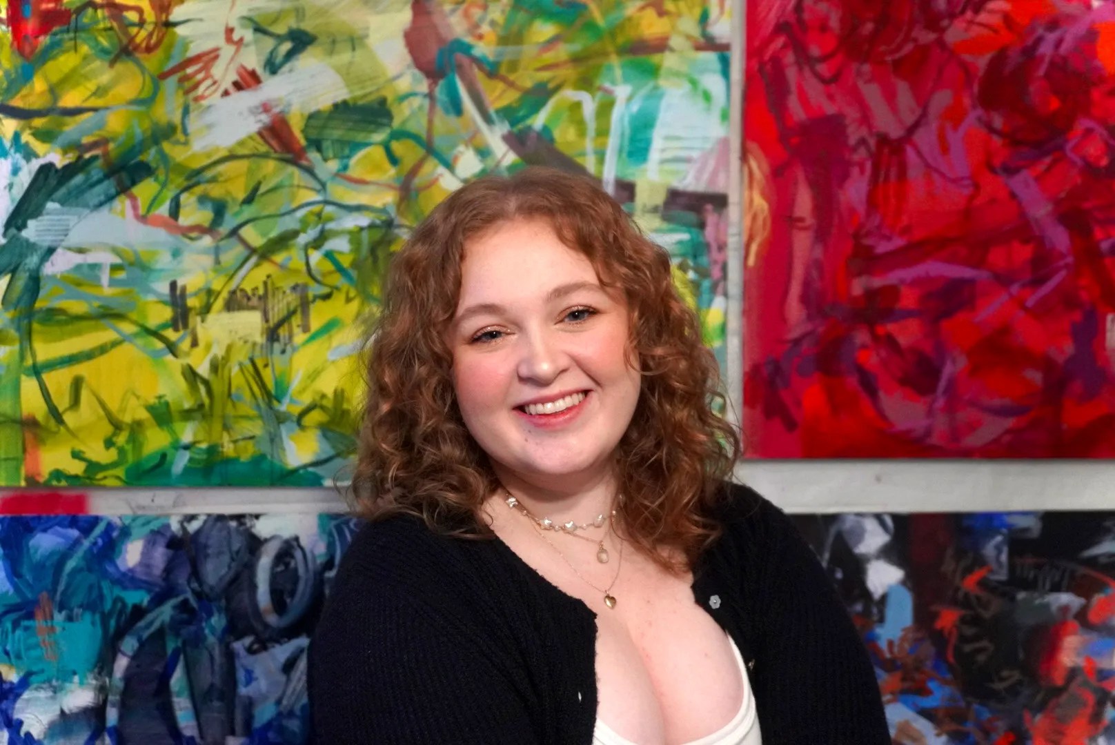 Smiling woman with curly hair in front of colorful abstract paintings.