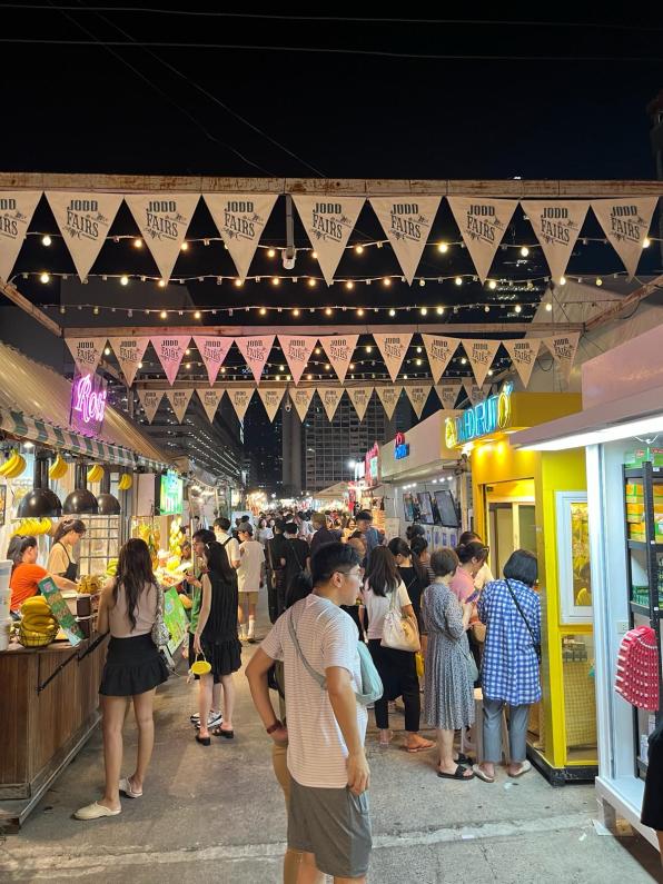 Banners across the JODD Night Market Bangkok Thailand with people in the stalls.