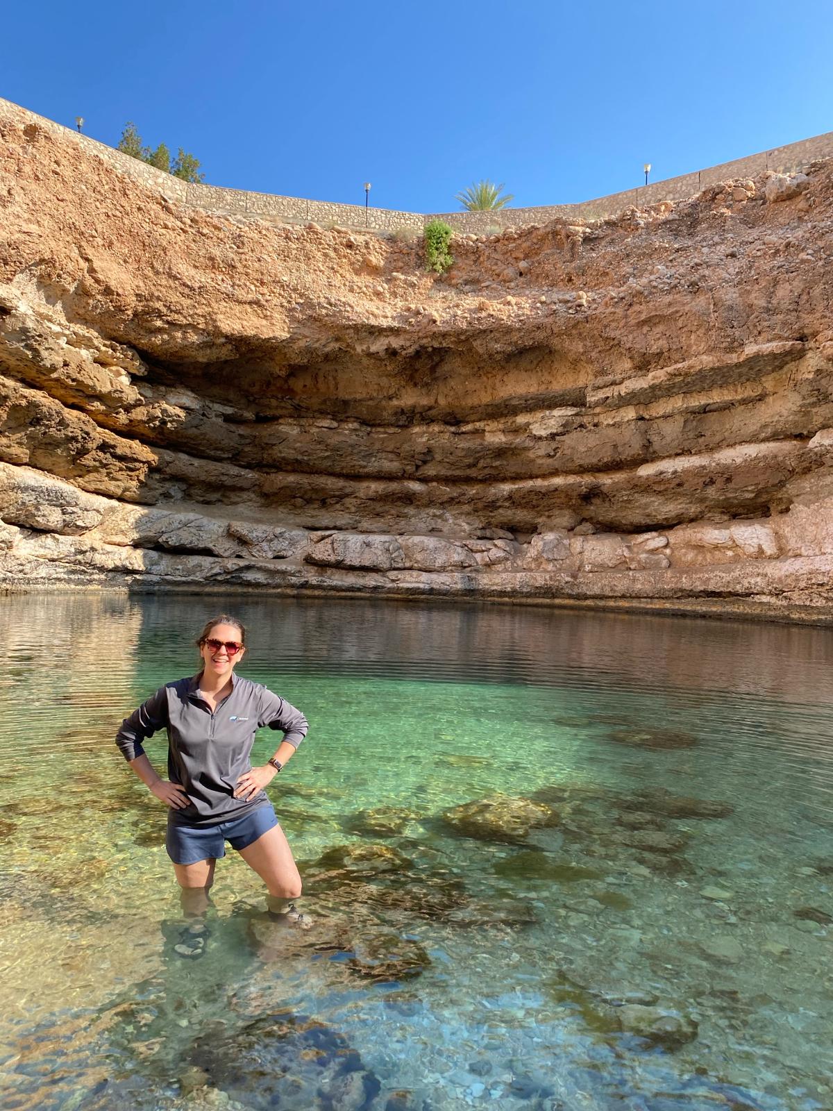 A lady smiling and standing in the Bimmah Sinkhole Oman with crystal clear water