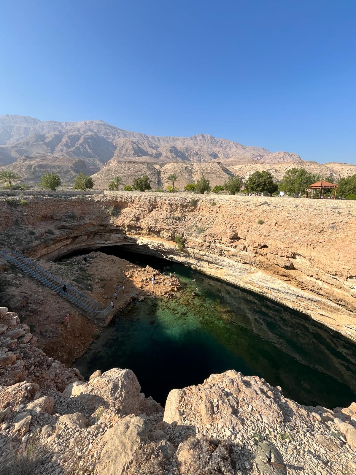 Bimmah Sinkhole with dark green waters below, the mountains and blue sky above. Oman