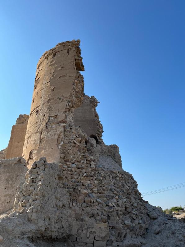 A broken tower in the old town of Birkat Al Mouz against a blue sky.