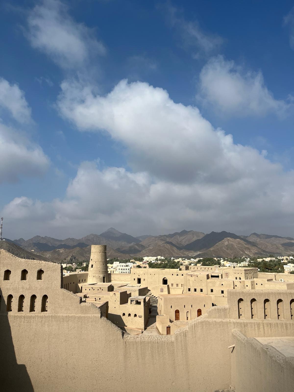 A Fort in the foreground with mountains, blue skies, and puffy white clouds.