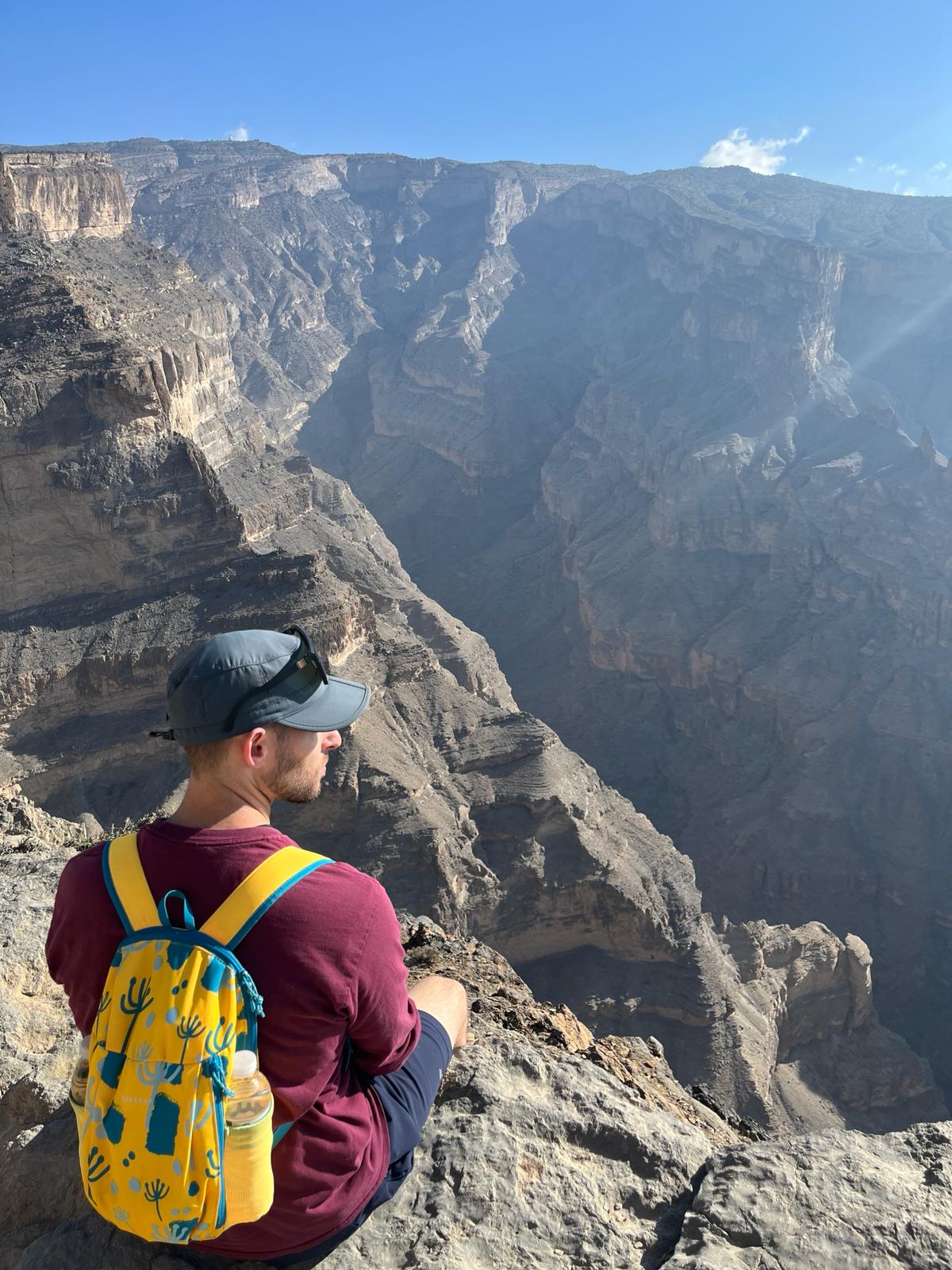 A man sitting on the side over looking the canyon on the W6 - Balcony Walk Hike Jabal Shams Oman