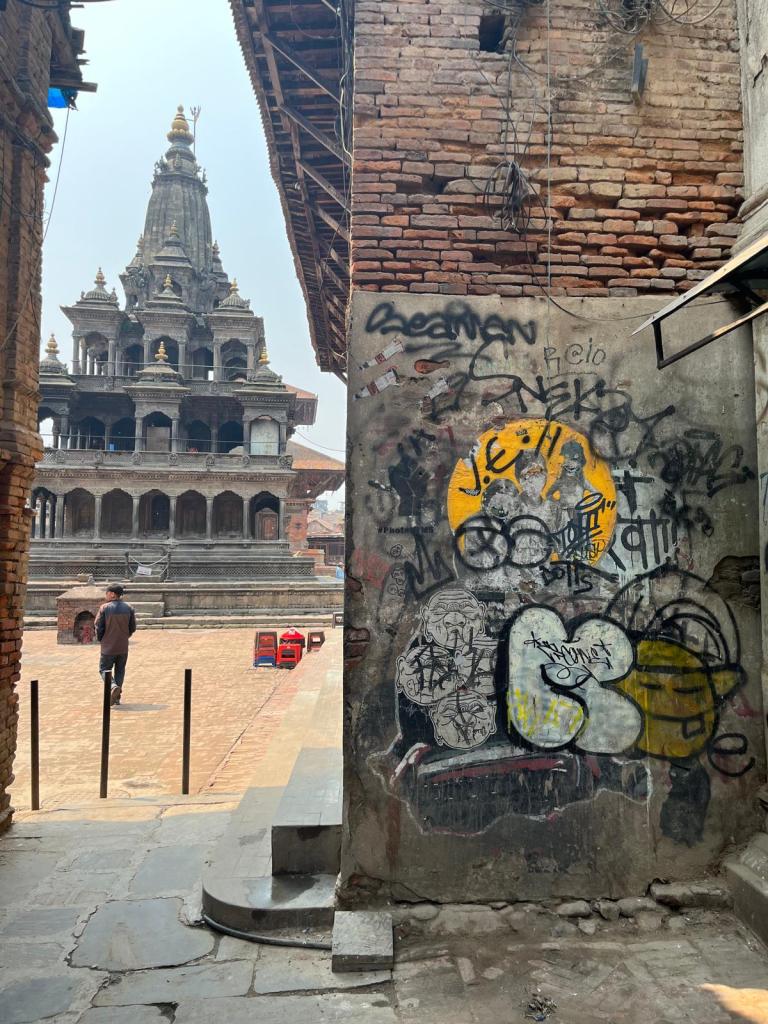 Patan Square Nepal with a temple in the background and a graffitied brick building