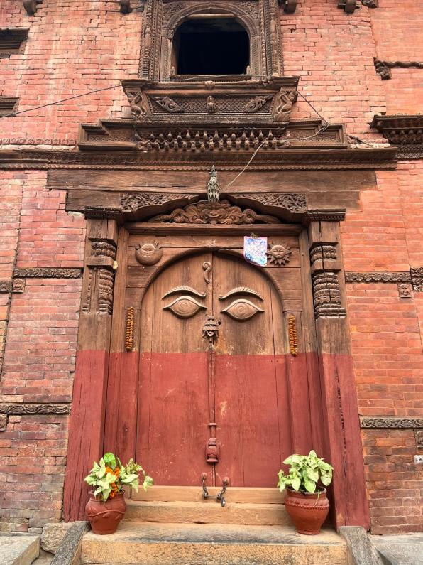 An ancient red wooden door with engraved eyes in a red brick building.