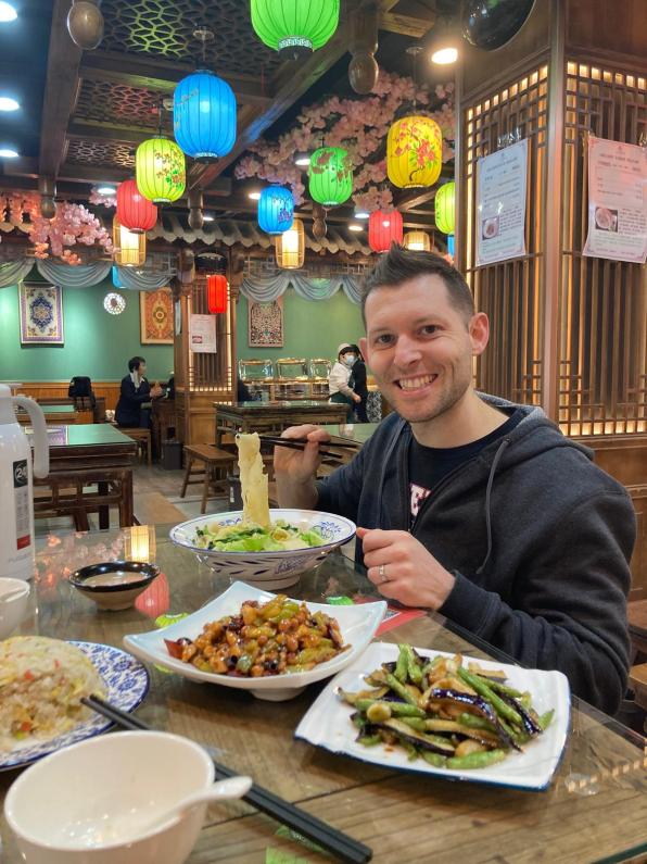 A man eating noodles, green beans, fried rice and kung pao chicken in a traditional Chinese restaurant