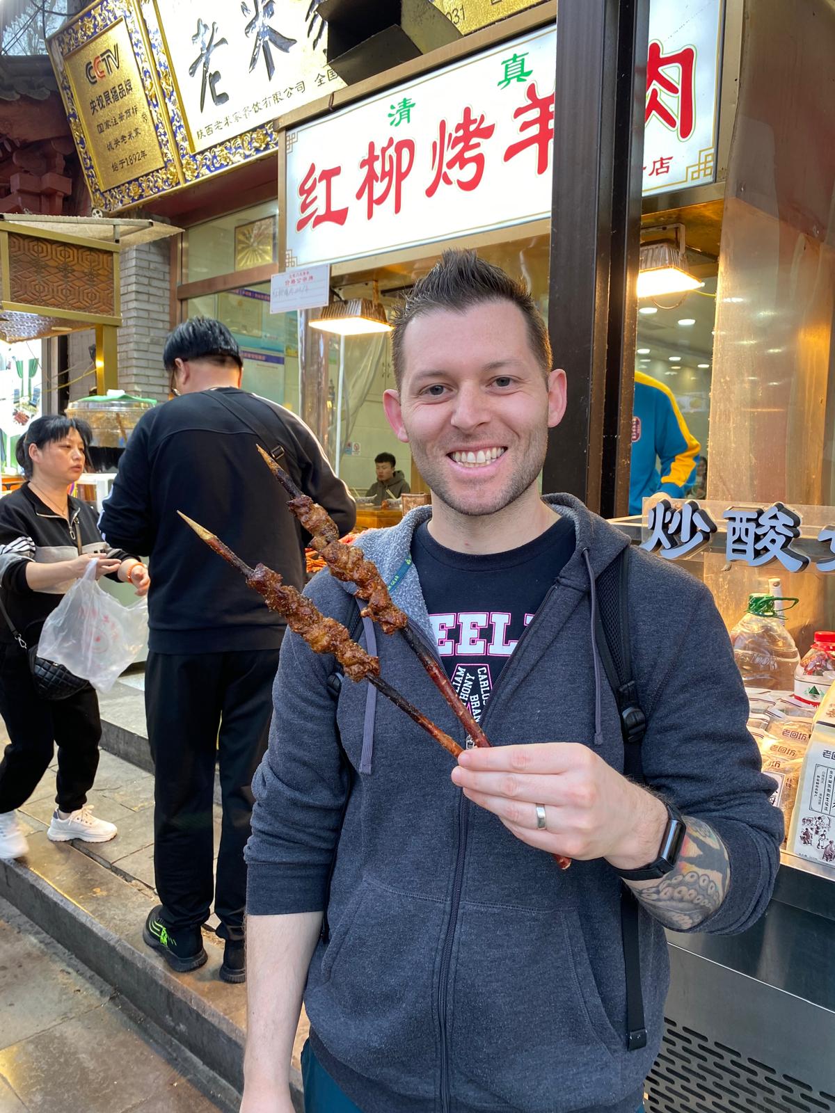 The Muslim Quarters walking food street with a man holding grilled lamb kebabs (chuan)