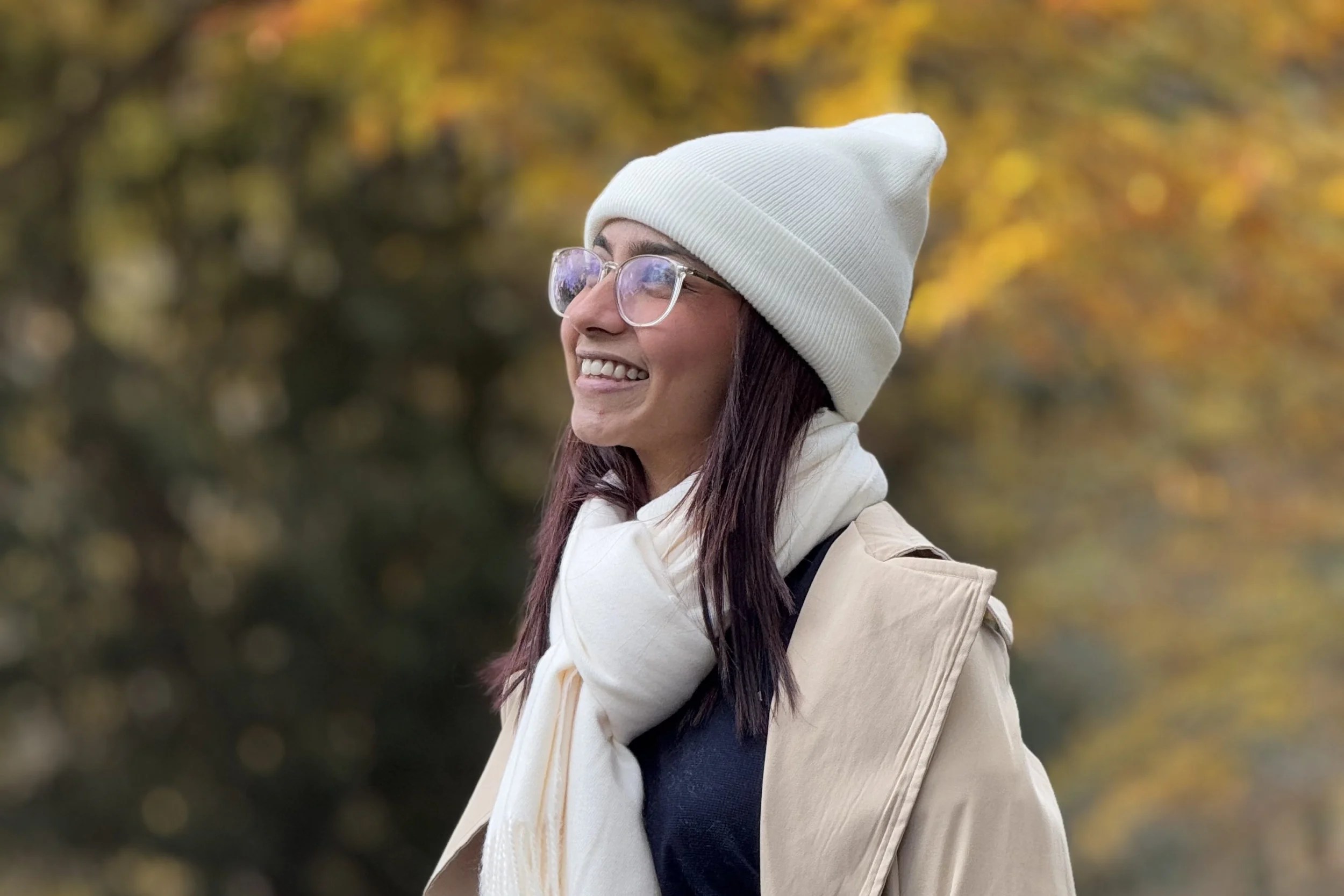 Dulangi smiling outdoors in autumn wearing a white hat and scarf