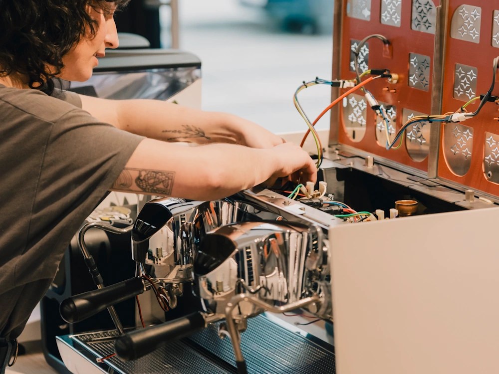 - Healthy Brew Hub A woman fixes an espresso machine in a coffee shop.