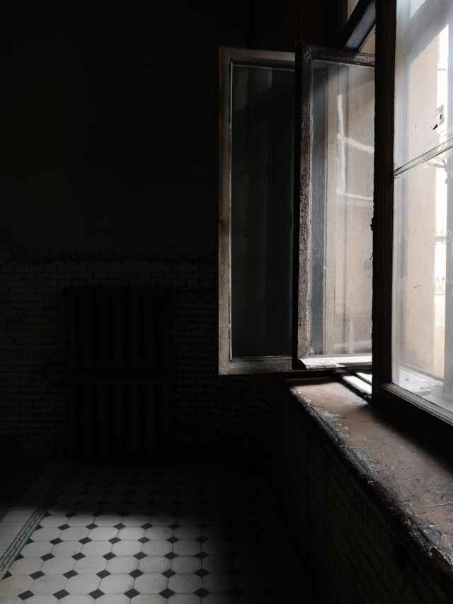 A dramatic indoor scene highlighting an open window with strong sunlight creating shadows on the floor.