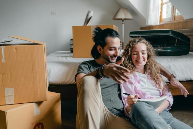 Happy couple sitting on the floor amidst moving boxes, planning their new home setup.