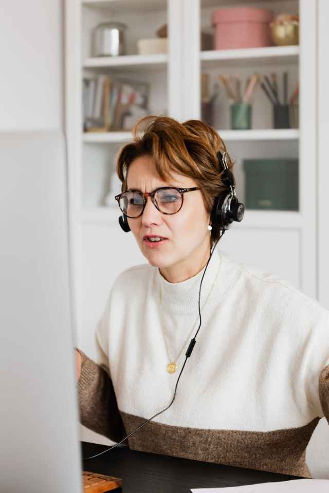 Focused woman with headphones on video call, working remotely from home office.