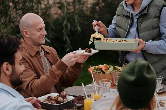 A group of friends enjoying a warm pasta meal outdoors, highlighting friendship and delicious food.