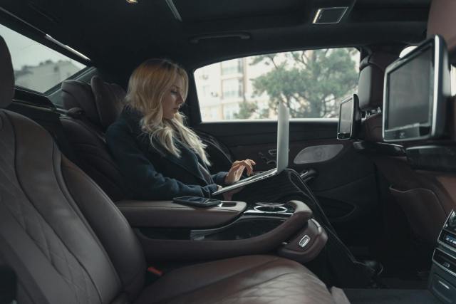 A businesswoman working on a laptop inside a luxury car, showcasing professionalism and modern technology.