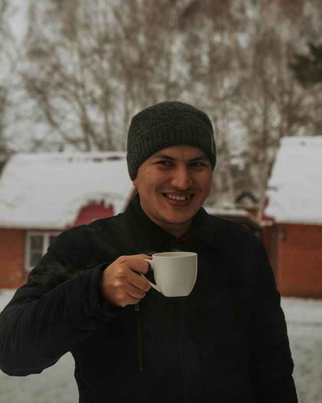 Smiling man holding a cup outdoors in snowy winter setting, dressed warmly.