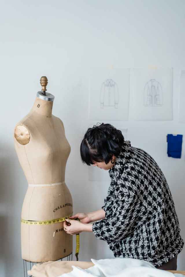 A fashion designer measures a mannequin in a studio, showcasing creative work in design and tailoring.