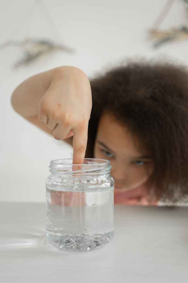 A child with curly hair focuses intently on a chemistry experiment involving a jar.